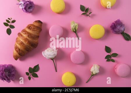 französisches Gebäck - Makronen und Croissant mit Blumen auf rosa Hintergrund. Draufsicht Stockfoto