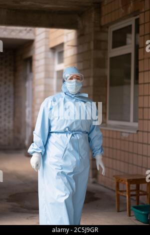 Weibliche Sanitäter in Schutzanzug, Maske und Schutzbrille geht aus dem Krankenhaus im Freien. Stadtkrankenhaus. Mai 2020, Brovary, Ukraine Stockfoto