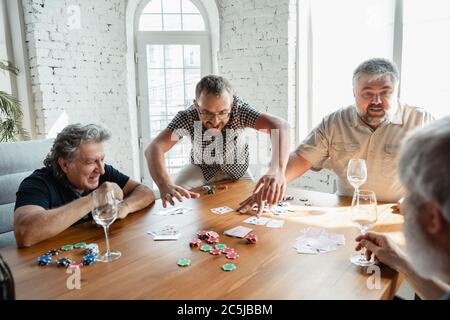Immer jung. Gruppe von glücklichen reifen Freunden Karten spielen und Wein trinken. Freuen Sie sich, aufgeregt. Kaukasische Männer spielen zu Hause. Aufrichtige Emotionen, Wohlbefinden, Gesichtsausdruck Konzept. Stockfoto