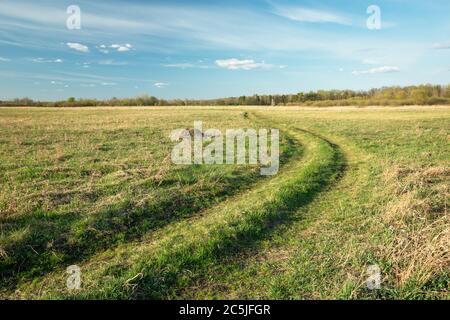 Eine kurvenreiche Straße in der Wiese und weiße Wolken am blauen Himmel, Blick bei sonnigem Tag Stockfoto