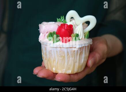 Frau Hand hält einen Cupcake mit schönen Rosen geformt Zuckerguss verziert Stockfoto