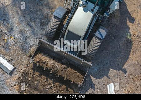 Bagger mit einem Eimer während der Grabung für den Bau der Straße. Bau der Straße mit speziellen Maschinen Stockfoto