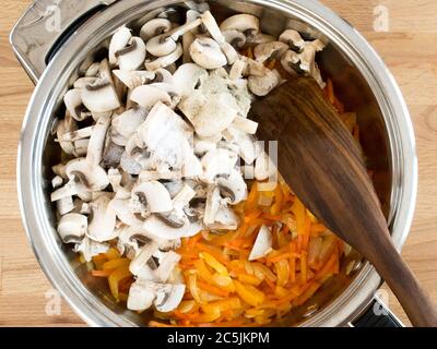 Champignons, Zwiebeln und Karotten in Scheiben geschnitten. Frittieren Sie die Speisen. Metallutensilien mit Zutaten, Draufsicht. Stockfoto