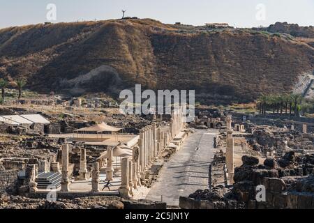 Israel, Bet She'an, Bet She'an Nationalpark, die Ruinen des römischen Cardo oder Hauptstraße, Palladius Street, in den Ruinen der Stadt Skythopolis, einer römischen Stadt im Norden Israels. Im Hintergrund ist Tel Bet She'an mit dem Standort der kanaanäischen Stadt Bet She'an auf seinem Gipfel. Stockfoto