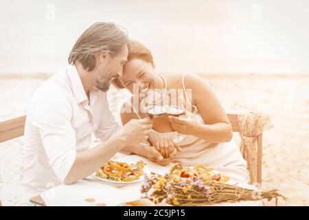 Charming Älteres Paar trinkt Wein am Meer. Zwei lächelnde Kaukasische Menschen verbringen Zeit zusammen in Strandcafé. Liebeskonzept. Jubiläumskonzept Stockfoto