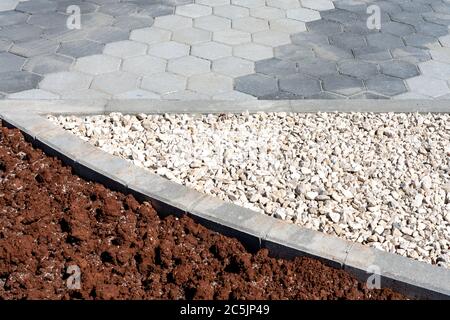 Grauer sechseckiger gepflasterter Pfad, der mit Kieselsteinen und Erde für spätere Bepflanzung geteilt ist. Stadtplanung. Stockfoto