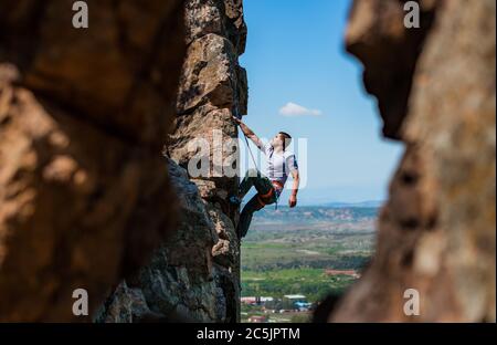 Junger Mann klettert auf einer felsigen Wand in einem Tal mit Bergen bei Sonnenaufgang Stockfoto