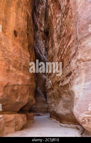 Jordanien, Petra, der schmale Schlitzschlucht, der Siq genannt wird, führt zu den Ruinen der nabatäischen Stadt Petra im Petra Archeological Park ist ein jordanischer Nationalpark und ein UNESCO-Weltkulturerbe. Im Vordergrund ist ein Teil des ursprünglichen Plattenbelades, mit Wasserkanälen in der Canyon Wand auf beiden Seiten geschnitzt. Stockfoto