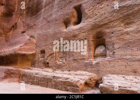 Jordanien, Petra, Nischen in der Wand der schmalen Schlitz Canyon namens Siq geschnitzt, die zu den Ruinen der Nabataean Stadt Petra im Petra Archeological Park führt ist ein jordanischer Nationalpark und ein UNESCO-Weltkulturerbe. Die Nischen enthalten Baetyls oder heilige Steinblöcke. Das gewölbte Baetyl in der Mitte ehrt den gott Dushara, während das nächste links davon eine andere Gottheit darstellt, Atargatis, die auf zwei Löwen steht. Die Schnitzerei ganz links soll die nabatäische dreifaltigkeit darstellen. Stockfoto