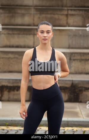 Eine sportliche junge Frau in Sportkleidung, die vor einer Reihe von Schritten steht und bereit für Bewegung ist. Stockfoto