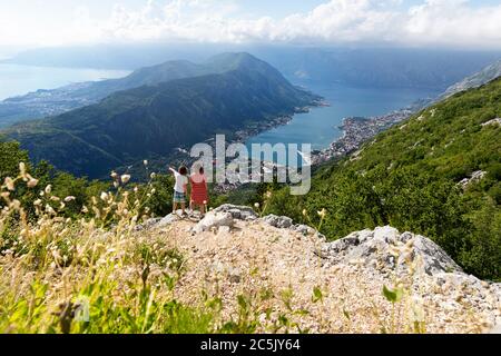 Mutter und Sohn stehen auf Felsen und zeigen in die Ferne mit Blick auf die Bucht von Kotor und Kotor, von der Straße nach Lovčen, Montenegro Stockfoto