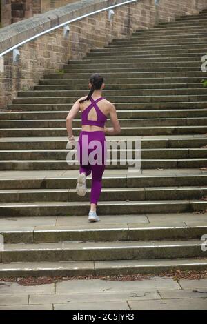 Eine Rückansicht einer jungen Frau in Sportkleidung, die Betonstufen hochläuft Stockfoto