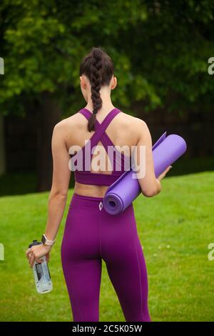 Eine Rückansicht einer athletischen jungen Frau in Leggings und Sport-BH mit einer Trainingsmatte Stockfoto