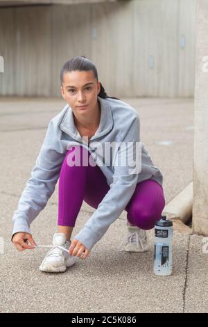 Eine attraktive Frau in Sportswear, die sich hinunterhocken und ihr Schnürsenkel binden Stockfoto