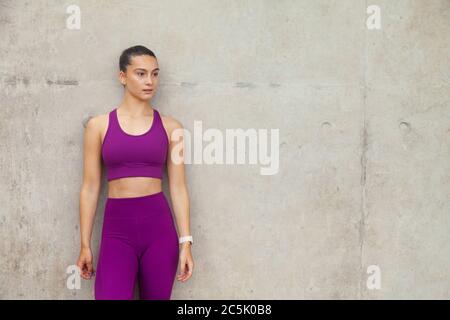 Eine attraktive Frau, die Sportkleidung trägt und sich an eine Betonwand lehnt. Stockfoto