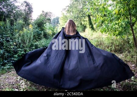 Ein Mädchen in einem schwarzen Umhang auf der Natur. Ein Mädchen in einer Kapuze. Gefahr.Fantasie Stockfoto