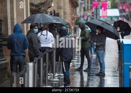 Glasgow, Schottland, Großbritannien. Juli 2020. Im Bild: Die Käufer warten geduldig, während sie sich in der Linie außerhalb des Apply Shops in der Buchanan Street sozial distanzieren. Buchanan Street Einkaufsviertel mit Einkäufern, die dem strömenden Regen trotzen, mit Regenschirmen und Gesichtsbezügen, die am 10. Juli nächste Woche obligatorisch werden. Quelle: Colin Fisher/Alamy Live News Stockfoto