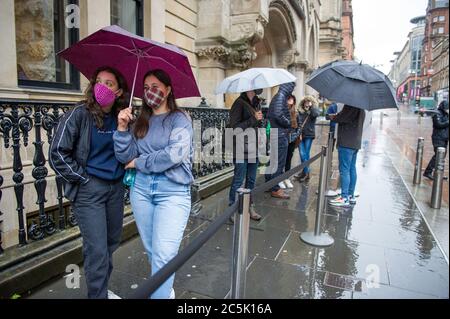 Glasgow, Schottland, Großbritannien. Juli 2020. Im Bild: Die Käufer warten geduldig, während die soziale Distanzierung den Apply Shop in der Buchanan Street übertraf. Buchanan Street Einkaufsviertel mit Einkäufern, die dem strömenden Regen trotzen, mit Regenschirmen Glasgow, Schottland, Großbritannien. Juli 2020. Im Bild: Buchanan Street Shopping-Bereich mit Käufern trotzen dem strömenden Regen mit Regenschirmen und Gesichtsbezügen, die am 10. Juli nächste Woche obligatorisch werden. Eine gelbe Warnung ‘sei bewusst’ wurde vom Met Office herausgegeben, die am Samstag um Mitternacht in Kraft tritt und bis Sonntag um 16 Uhr dauert.Quelle: Colin Fisher/Alamy Live News Stockfoto