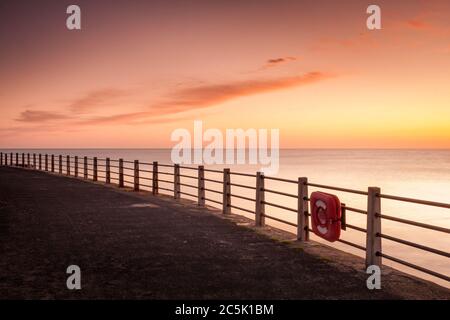 Eine ruhige, warme und farbenfrohe Aussicht über den Strand und die Bucht, die zum Horizont blickt und rollende Wellen auf den Strand waschen. Stockfoto