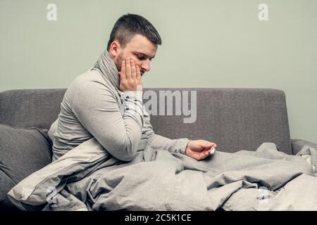 Krankheit. Heitern Sie zu Hause. Ein junger Mann ist krank, wird zu Hause behandelt. Bläst ihre Nase in eine Serviette, laufende Nase. Körpertemperaturmessung. Infektion Stockfoto