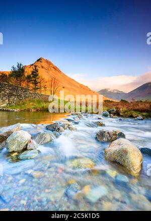 Zwischen den Felsen am Wastwater Ufer stehend, Blick zurück zur Overbeck Brücke & die letzte der Wintersonne auf der Bergkette. Stockfoto