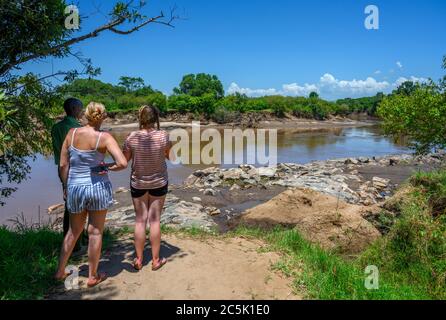 Touristen und Park Ranger Blick auf Nilpferde und Krokodile in der Mara River, Mara Dreieck, Masai Mara National Reserve, Kenia, Ostafrika Stockfoto