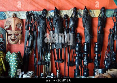 Handgemachtes oder handgemachtes afrikanisches Souvenir Traditionelle afrikanische primitive Figur im Makonde Stil und andere Souvenirs, die in einem Marktstand verkauft werden. Kendwa Stockfoto