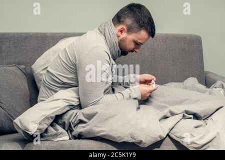 Krankheit. Heitern Sie zu Hause. Ein junger Mann ist krank, wird zu Hause behandelt. Bläst ihre Nase in eine Serviette, laufende Nase. Körpertemperaturmessung. Infektion Stockfoto