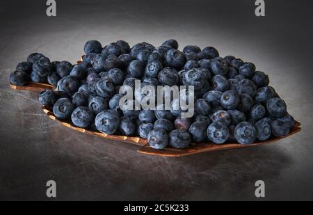 Holzschale mit frischen Heidelbeeren auf silbernem Hintergrund, stilisiert Stockfoto