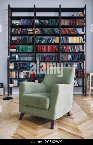 Grüner Stuhl im Innenraum. Bücherregal mit alten Büchern auf den Regalen. Bücher in einem alten Holzschrank Stockfoto