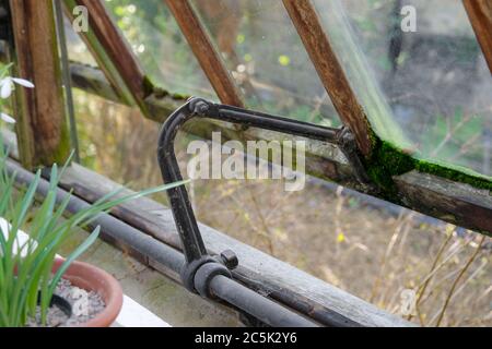 Aufklappbare offene Holzgartenfenster mit dem kunstvollen, eisernen Scharnier-System. Wird verwendet, um bei der Belüftung in einem feuchten und warmen Gewächshaus zu helfen. Stockfoto