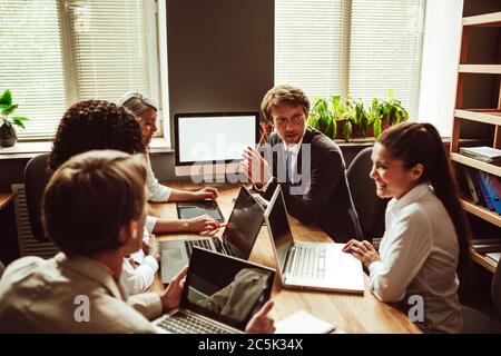 Teamarbeit von verschiedenen Gruppen, die am Verhandlungstisch mit Computern darauf sitzen. Diskussion oder Brainstorming von Geschäftsleuten in modernen Büros. Getönte Stockfoto