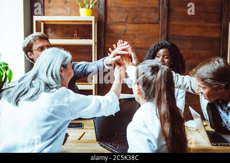 Nach erfolgreichem Brainstorming gehen verschiedene Gruppen Hand in Hand. Das Büroteam schloss sich in Einheit an und gab freudig fünf hohe Gesten zueinander Stockfoto