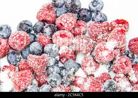 Eine Beerenmischung in Zucker aus gefrorenen Himbeeren und Blaubeeren. Ein gefrorene Beeren mit Zucker. Ein süßer Hintergrund mit gefrorenen Himbeeren und Heidelbeeren Stockfoto