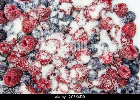 Eine Beerenmischung in Zucker aus gefrorenen Himbeeren und Blaubeeren. Ein gefrorene Beeren mit Zucker. Ein süßer Hintergrund mit gefrorenen Himbeeren und Heidelbeeren Stockfoto