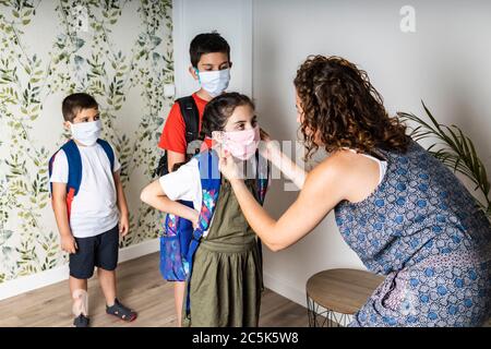 Mutter setzt ihren Kindern Gesichtsmasken auf, bevor sie zur Schule gehen Stockfoto