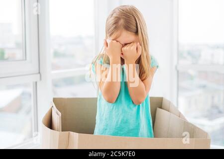 Modeling kleines Mädchen zeigt Ausdrücke, bedeckt Gesicht mit ihren Händen, in der Box stehen Stockfoto