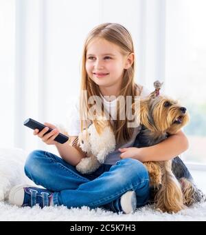 Nettes Mädchen und ihr Hund wechseln Kanäle mit tv-Fernbedienung Stockfoto