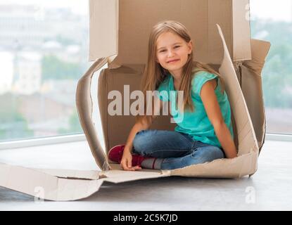 Lächelndes Schulmädchen sitzt in zerrissenen Versandkarton Stockfoto