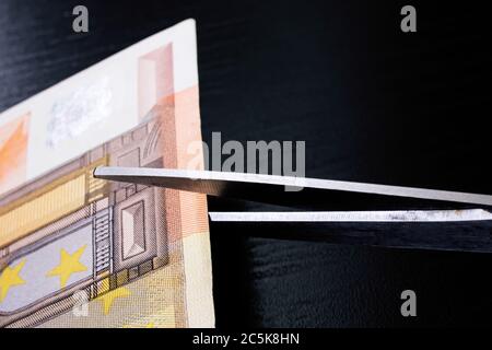 Schere schneiden eine Euro-Rechnung Nahaufnahme auf schwarzem Hintergrund Stockfoto