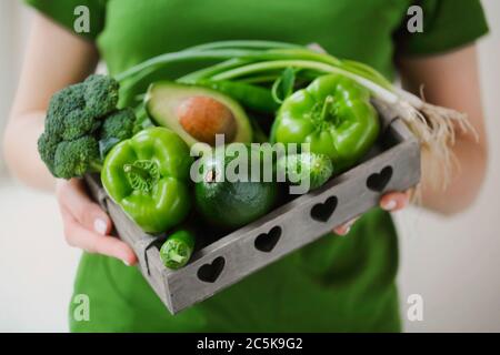 Hoher Winkel von anonymen Weibchen in grünen T-Shirt zeigt Container mit reifen gesunden Gemüse Stockfoto