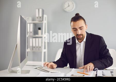 Der Geschäftsmann in einer schwarzen Jacke funktioniert. Analysen am Computer im Büro. Stockfoto