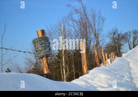 Haspel Stacheldraht auf einem hölzernen blass, Teil halb fertig Stacheldraht Zaun neben schneebedeckten Fußweg Stockfoto