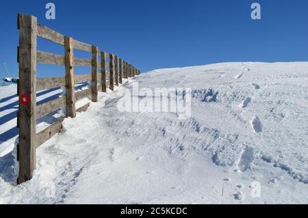 Holzzaun auf einer verschneiten Pisten auf Skigebiet, mit roten und weißen Markierung auf einer Säule Stockfoto