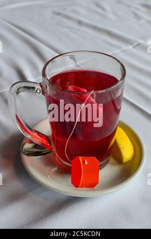 Filtertüte Hibiskustee in einem Glas auf weißem, keramischem Untertasse mit Zitronenscheibe Stockfoto