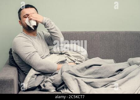 Krankheit. Zu Hause erfreuen. Ein junger Mann ist krank, ist zu Hause behandelt. Bläst ihre Nase in eine Serviette, laufende Nase. Infektion, Epidemie, Bacillus Träger. Stockfoto