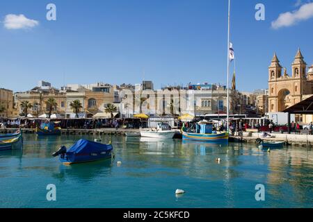 MARSAXLOKK, MALTA - 31. DEZEMBER 2019: Marsaxlokk Markt mit traditionellen Luzzu Fischerbooten an einem schönen Wintertag mit blauem Himmel und grünem Meer Stockfoto