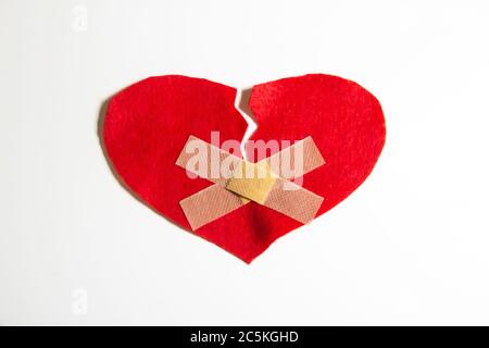 Gebrochenes Herz und mit einem Pfand zusammengeklebt. Ein Herz aus Filz. Ein Konzept über gebrochene Liebe. Herz mit Gips isoliert auf weißem Hintergrund Stockfoto