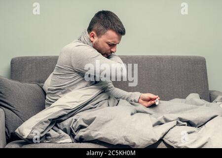 Krankheit. Heitern Sie zu Hause. Ein junger Mann ist krank, wird zu Hause behandelt. Bläst ihre Nase in eine Serviette, laufende Nase. Körpertemperaturmessung. Infektion Stockfoto