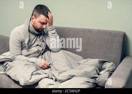 Krankheit. Heitern Sie zu Hause. Ein junger Mann ist krank, wird zu Hause behandelt. Bläst ihre Nase in eine Serviette, laufende Nase. Körpertemperaturmessung. Infektion Stockfoto